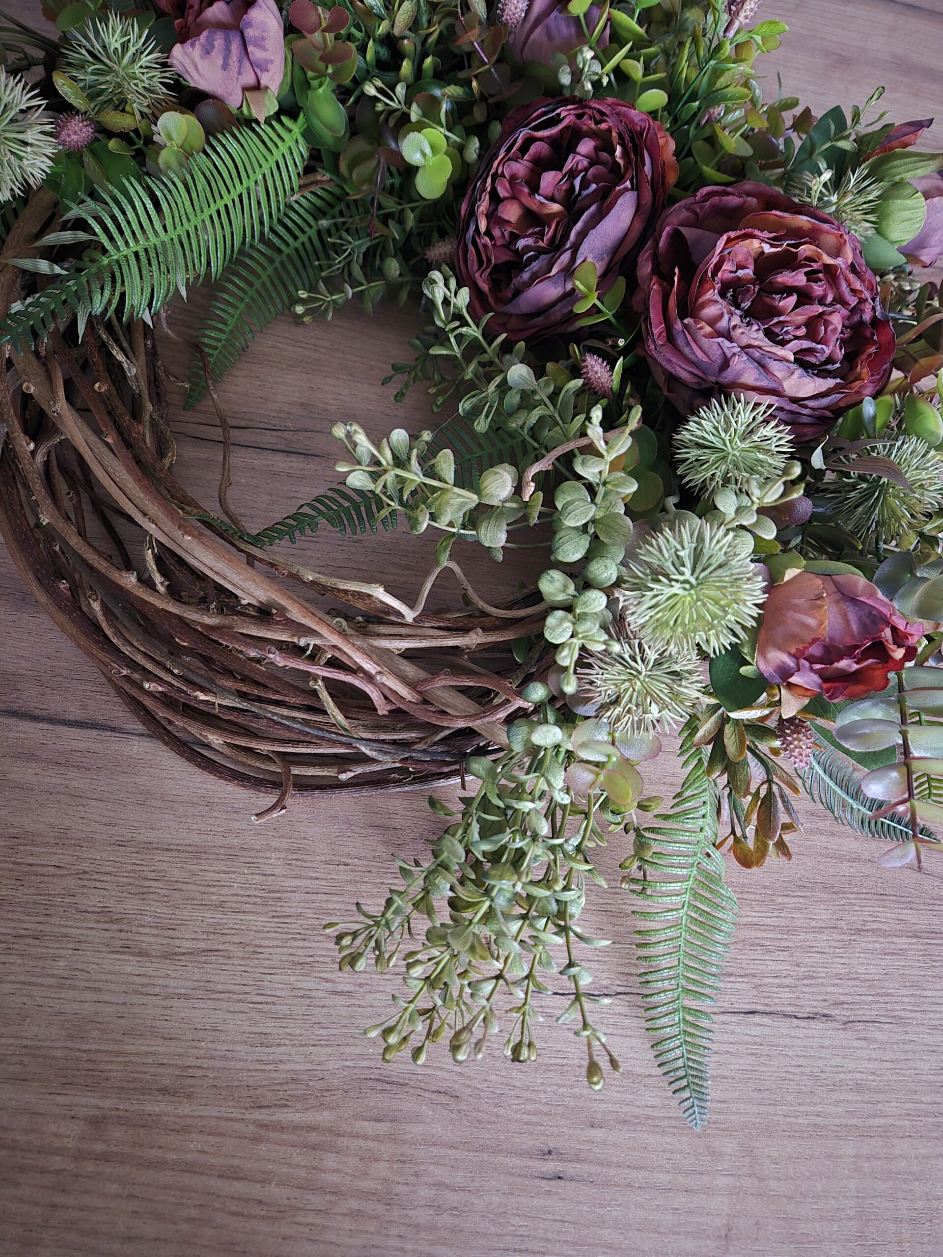 Wianek jesienny z różami i zielenią - zbliżenie na plecioną obręcz.